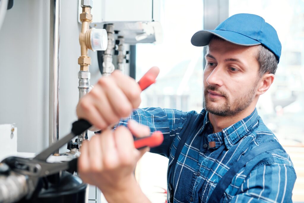 plumber in a ball cap using a wrench to tighten a pipe