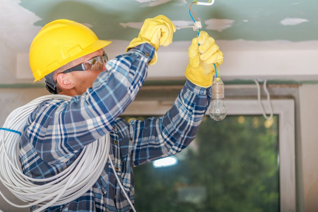 Electrician wiring the ceiling in a yellow hardhat