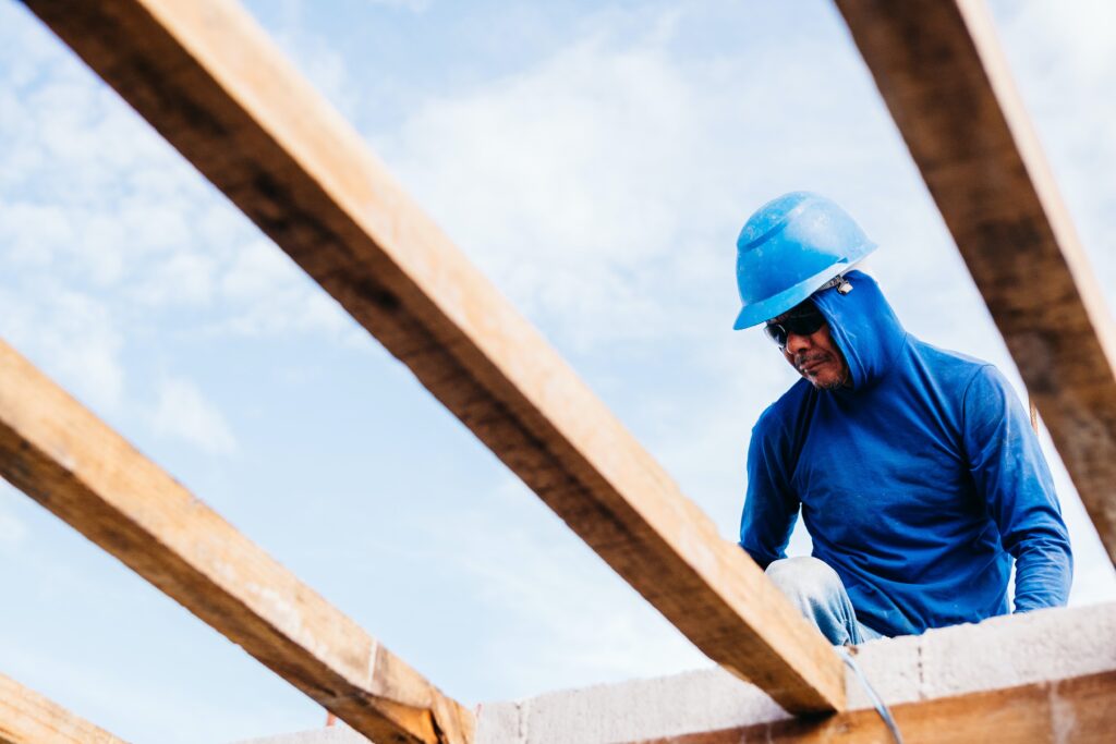 Roofer in a blue hard hat working on top of a roof