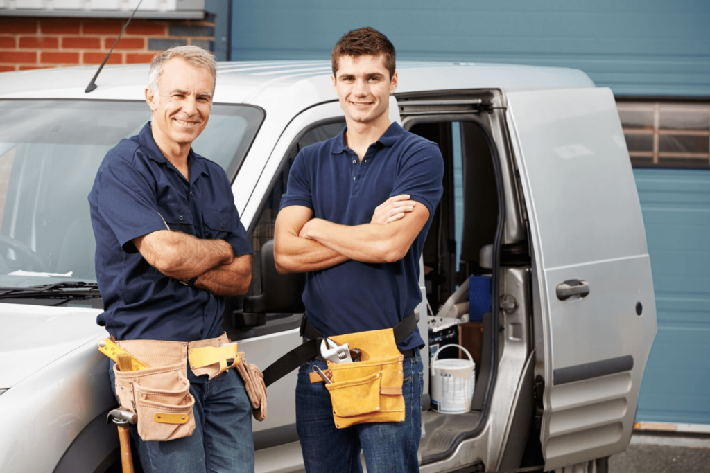 a dad and son in tool belts in front of a work van